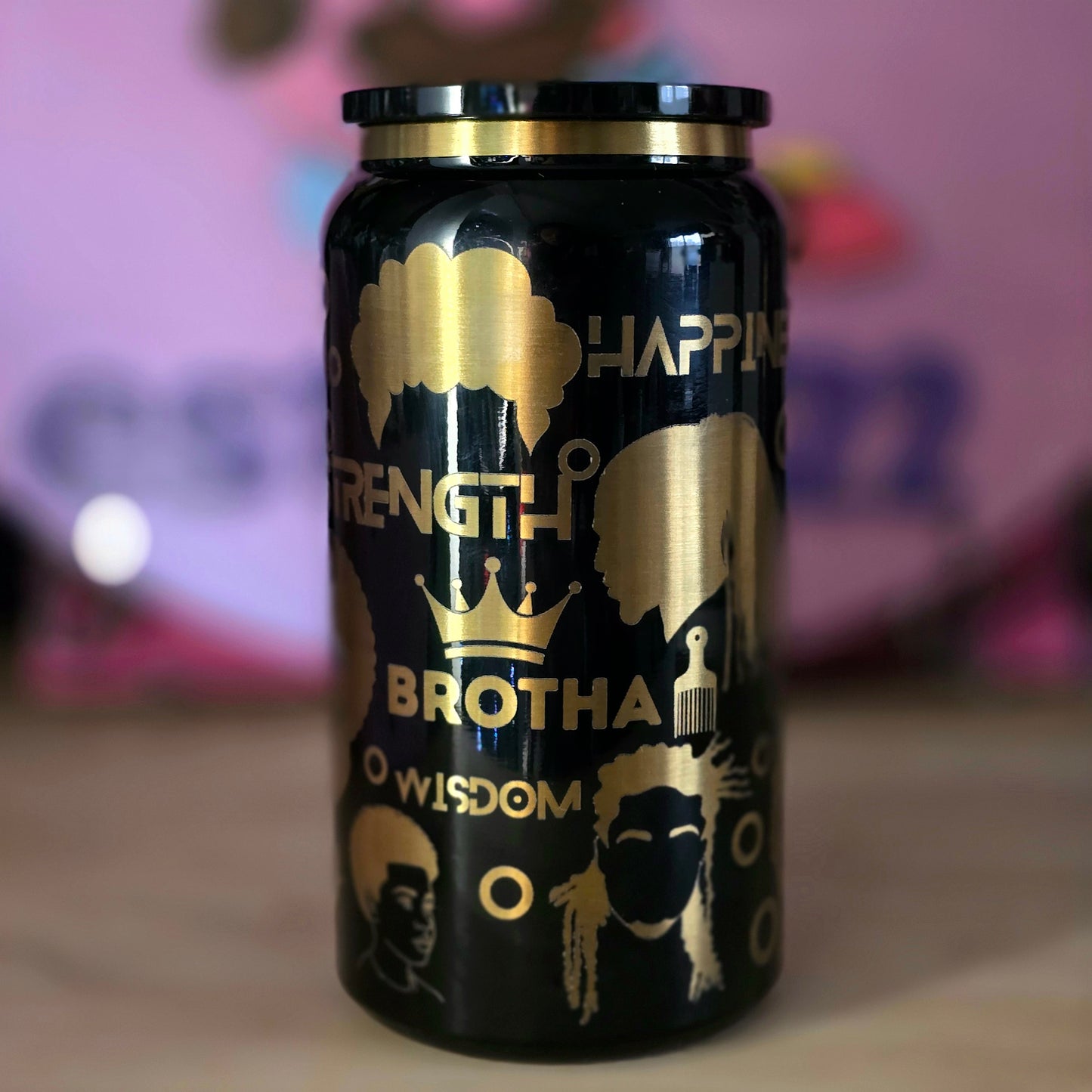 Black tumbler with gold text and graphics on a blurred background